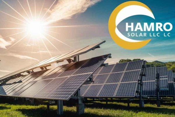 Solar panels in a green field absorbing sunlight under a clear blue sky, with the logo of "Hamro Solar LLC" displayed prominently in the top right corner.